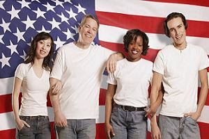 Four diverse adults smiling in front of a U.S. flag.