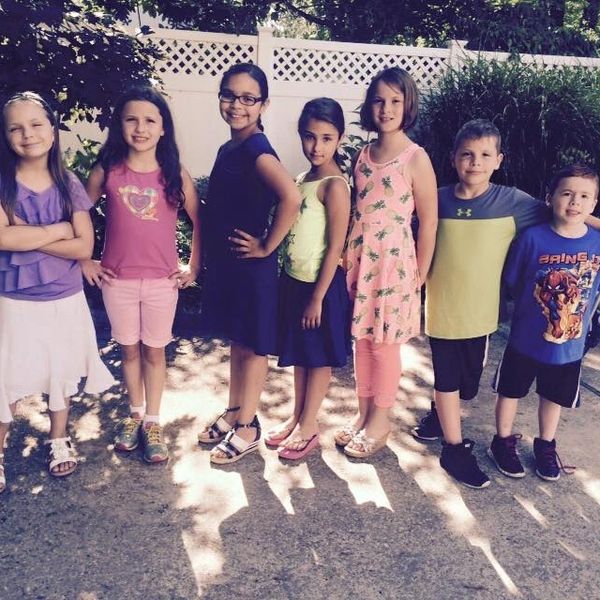 Seven children standing in a row outdoors, smiling at the camera.