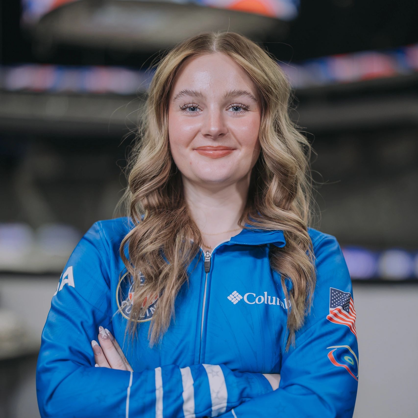 Confident young woman in a blue Columbia jacket with USA flag patch.