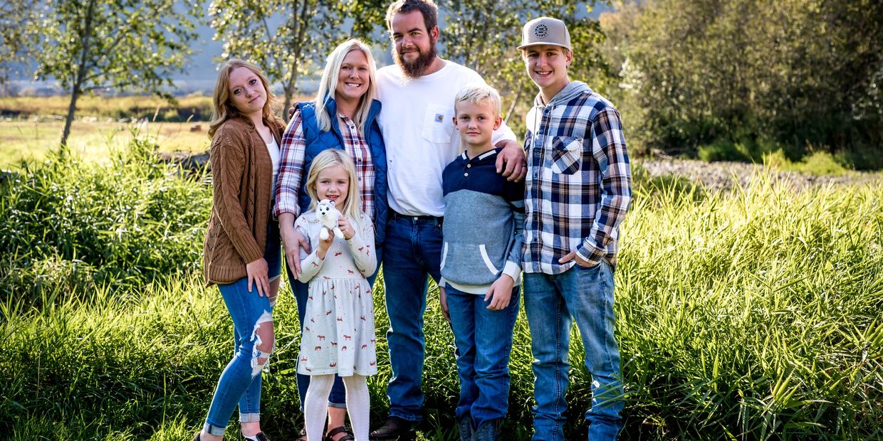 A happy family of six posing outdoors in a sunny, grassy field.