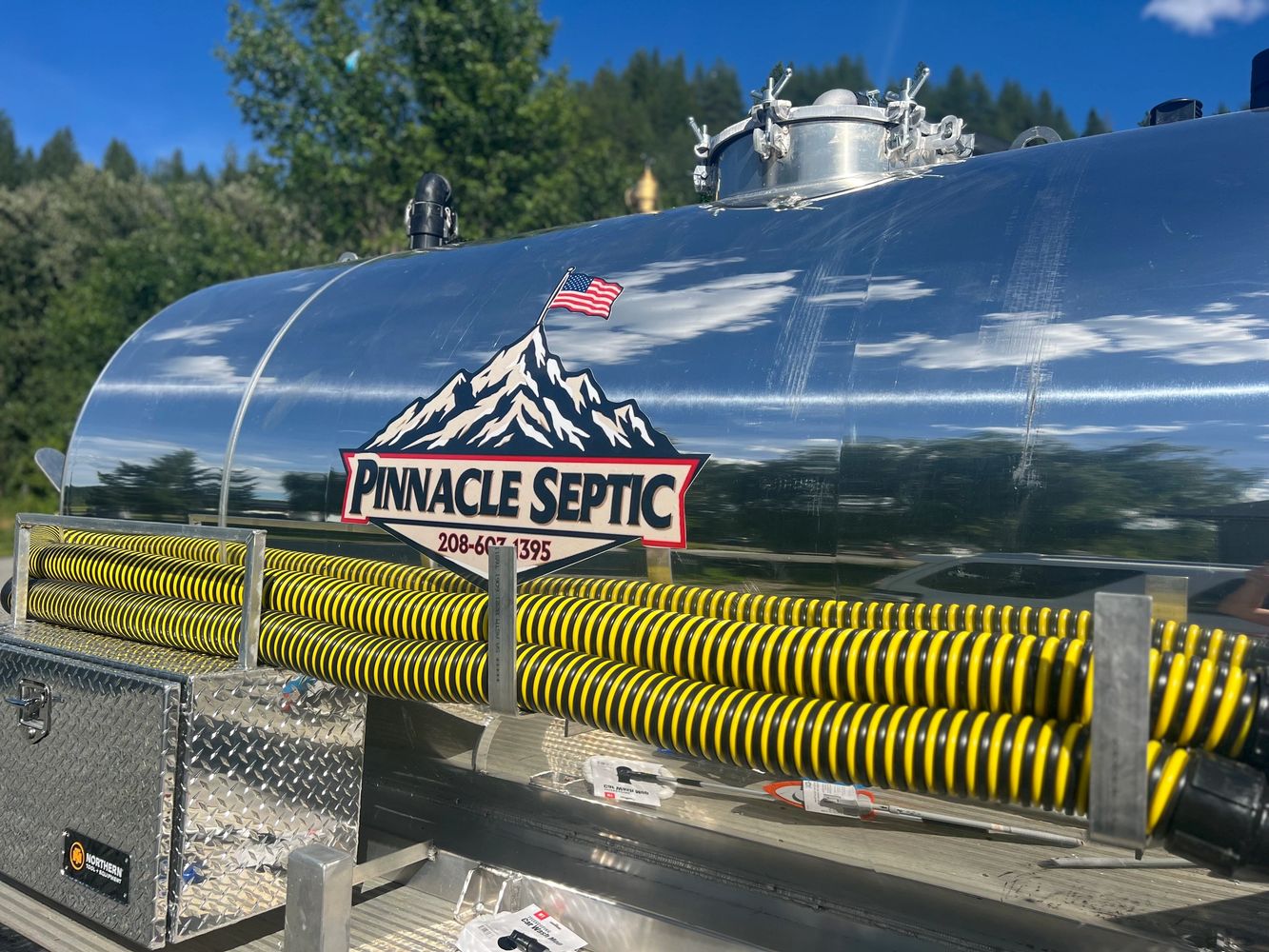 Shiny septic service truck with yellow hoses and a mountain logo.