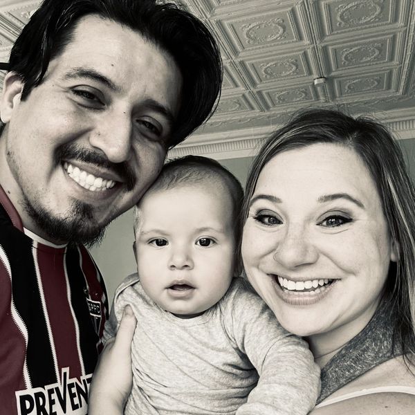Happy family selfie with parents and baby smiling together indoors.