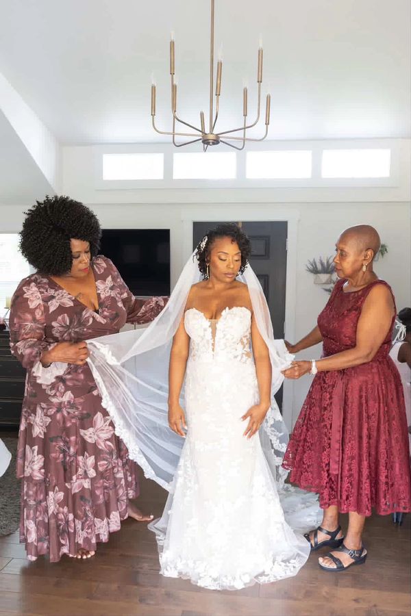 Real Bride Shayla in a strapless, fitted lace wedding dress surrounded by her mother and grandmother