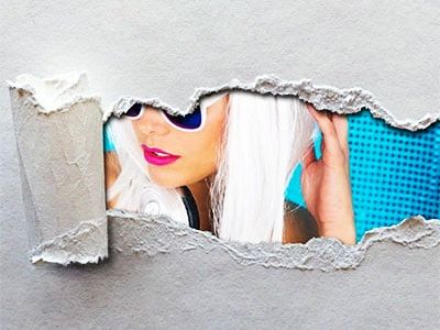 Woman with white hair and sunglasses peeking through torn paper.