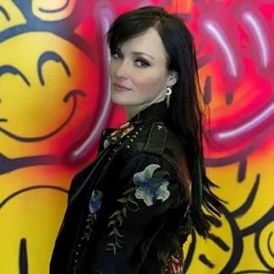 Woman posing in front of colorful graffiti with smiley faces.
