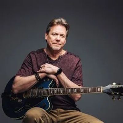 Man sitting with an electric guitar against a dark background.