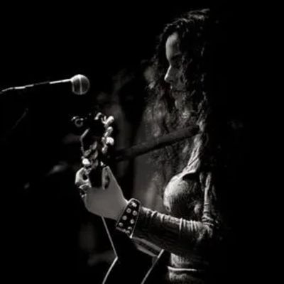 Black and white image of a woman playing guitar near a microphone.