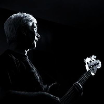 Elderly man playing bass guitar in dramatic lighting.