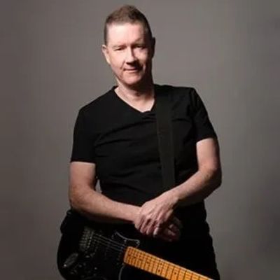 Man in black shirt holding electric guitar against gray background.