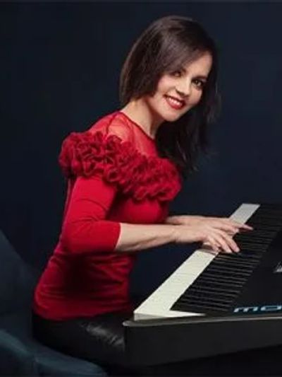 Woman in a red top playing keyboard with a smile.