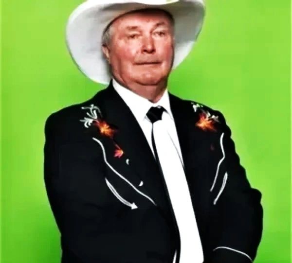 Man in a white cowboy hat and embroidered black jacket against a green background.