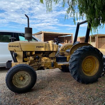 Yellow Ford 260C tractor parked outdoors near vehicles and wooden structures.