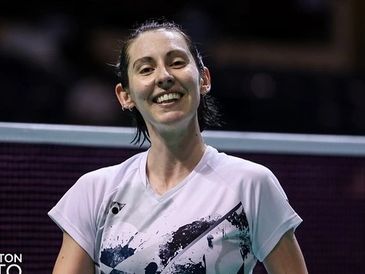 Smiling badminton player in white sportswear on court.