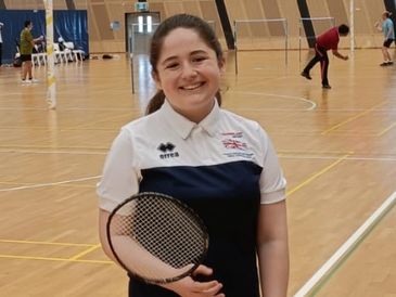 Smiling girl holding a badminton racket on an indoor court.