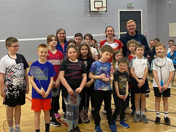 Group of children and adults posing with badminton rackets in a gymnasium.
