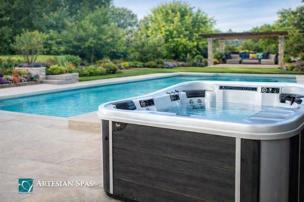 Modern hot tub beside a swimming pool in a lush backyard.