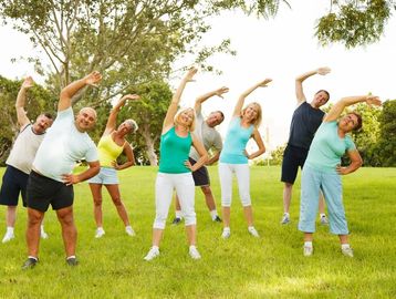 A group of people exercising outdoors with side stretches on a grassy field.