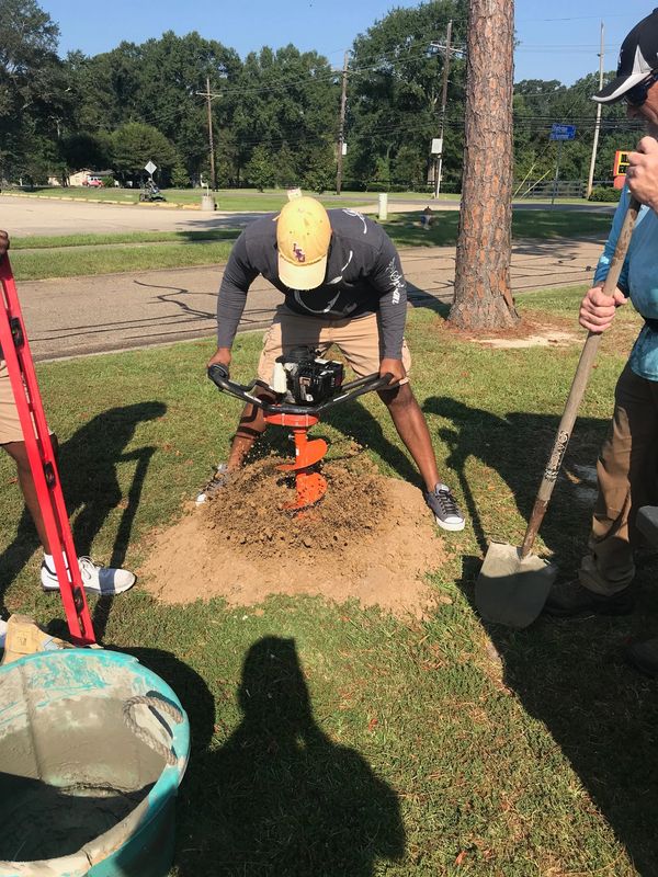 Man operating an orange earth auger to dig a hole in the ground.