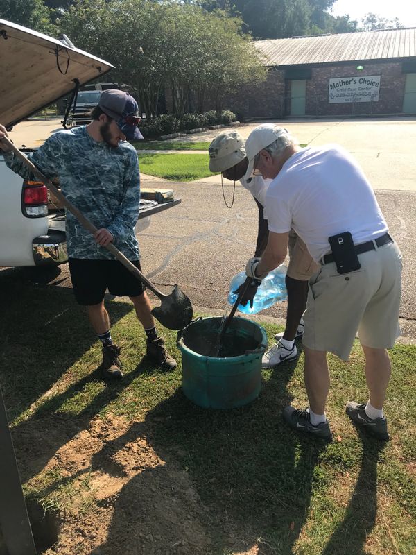 Three men mixing cement outdoors using a shovel and water.