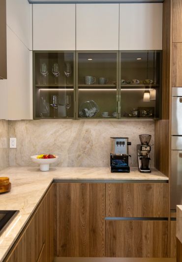 Modern kitchen corner with wood cabinets, marble countertops, and coffee appliances.