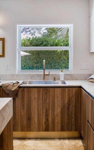Modern kitchen sink area with wooden cabinets and a large window overlooking greenery.