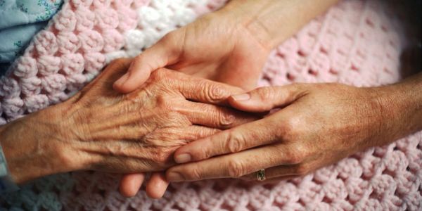 Two hands gently holding each other on a pink blanket.