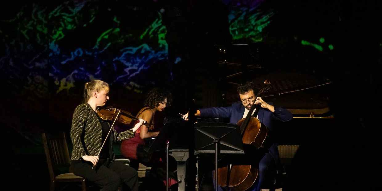 Trio performing classical music on stage with colorful background.