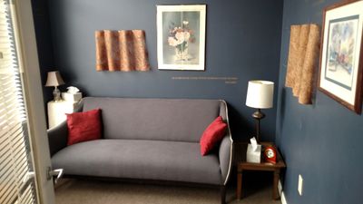 A cozy room with a gray couch, red pillows, and framed artwork on blue walls.