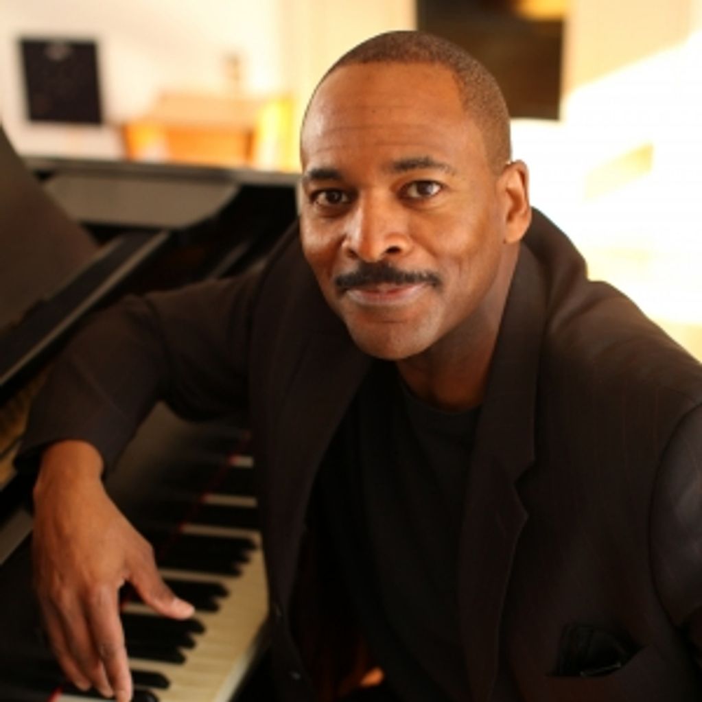 Man smiling warmly by a piano keyboard.