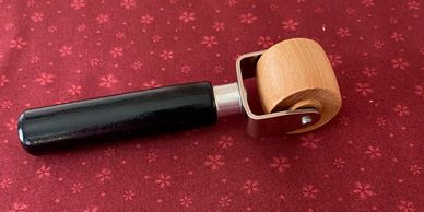 A wooden roller tool with a black handle on red patterned fabric.
