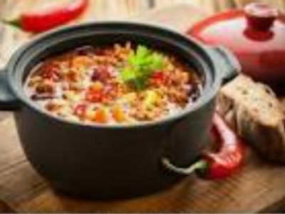 Hearty chili served in a black pot with bread and chili pepper.