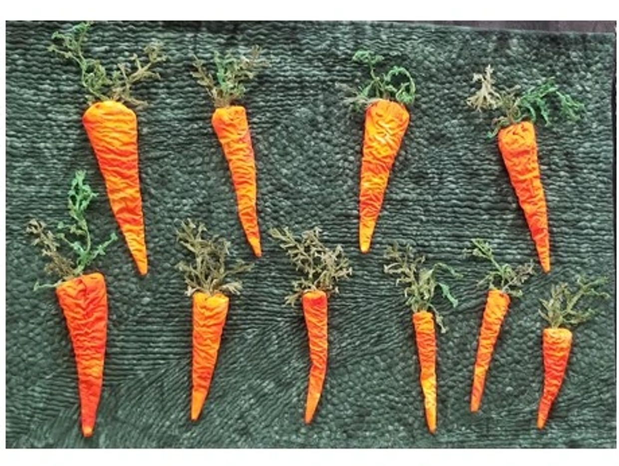 Handcrafted fabric carrots with leafy tops on a textured green surface.