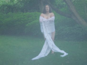 A person wrapped in a long white cloth stands in a misty garden.