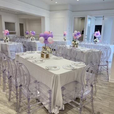 Elegant event setup with transparent chairs and pastel balloon centerpieces.