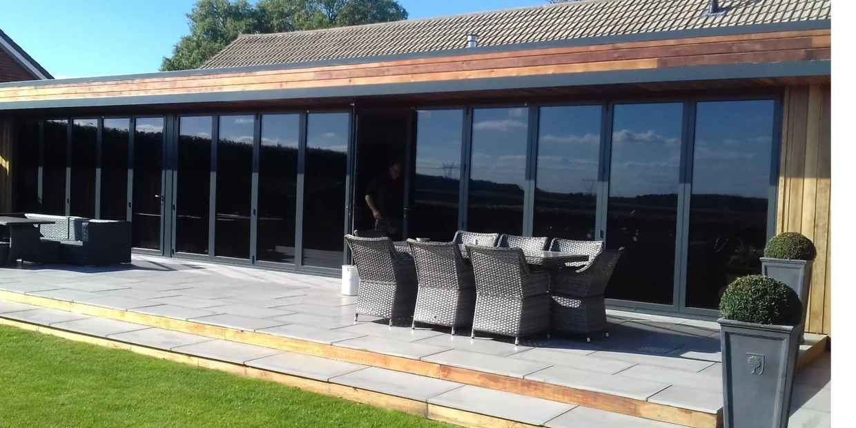 Modern patio with wicker furniture and large aluminium bi-fold door with glass doors on a sunny day in Sheffield.