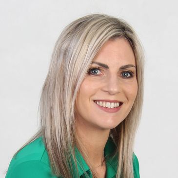 Smiling woman with blonde hair wearing a green top against a plain background.