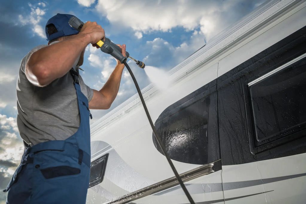 A person pressure washing a large vehicle.