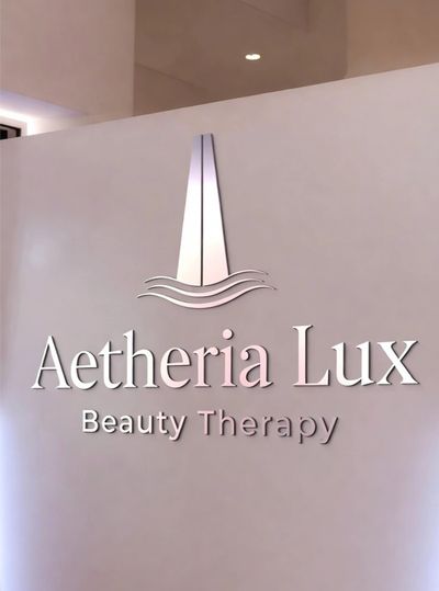 Aethria Lux Beauty Therapy logo on a soft pink wall.
