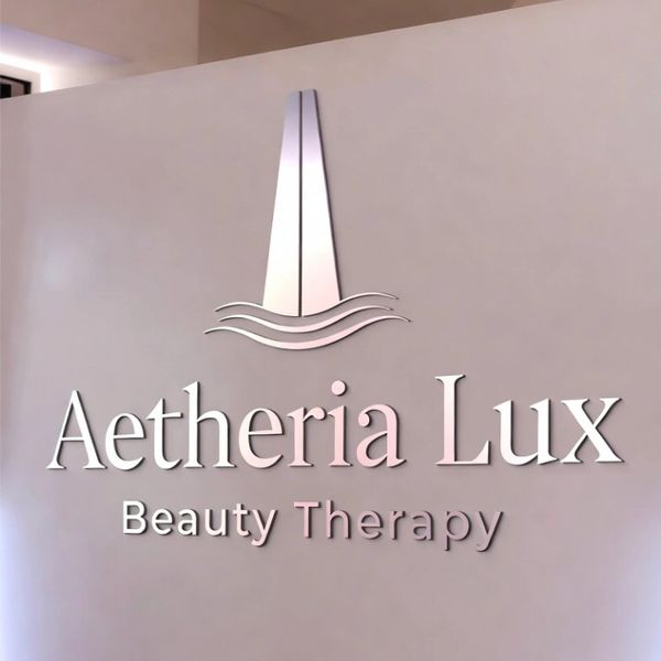 Aethria Lux Beauty Therapy logo on a soft pink wall.