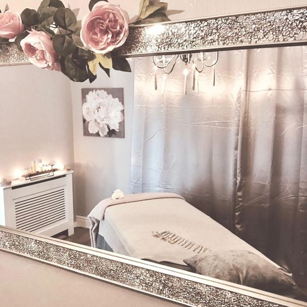 Cozy spa room with a massage table, soft lighting, and floral decor.