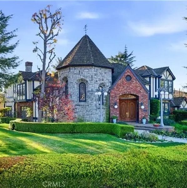 A charming Tudor-style house with stone and brick facade surrounded by manicured greenery.