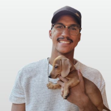 Man smiling and holding a small brown puppy.