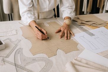 Person drafting a sewing pattern on paper with tools.