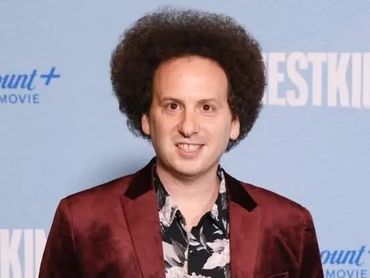 Man with afro hairstyle in maroon blazer and floral shirt.