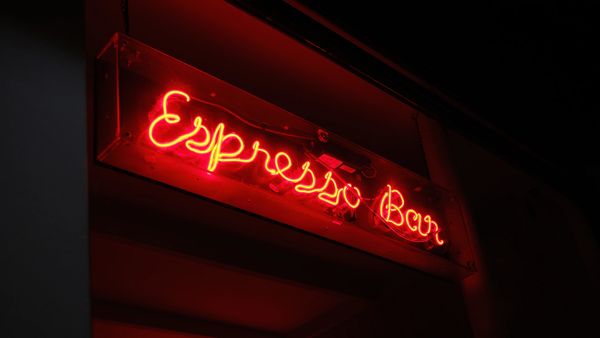 
The image shows a vibrant red neon sign that spells out "Espresso Bar" in a flowing, cursive script