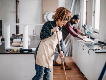 A man and a woman cleaning up after construction work in a kitchen.