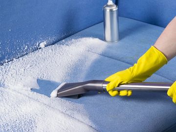 A person with yellow gloves cleaning a sofa.