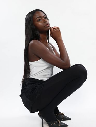 Young woman in black tights and heels, posing thoughtfully against a white background.