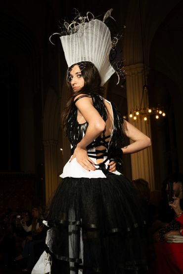 Model wearing avant-garde black and white dress with tall headpiece on runway.