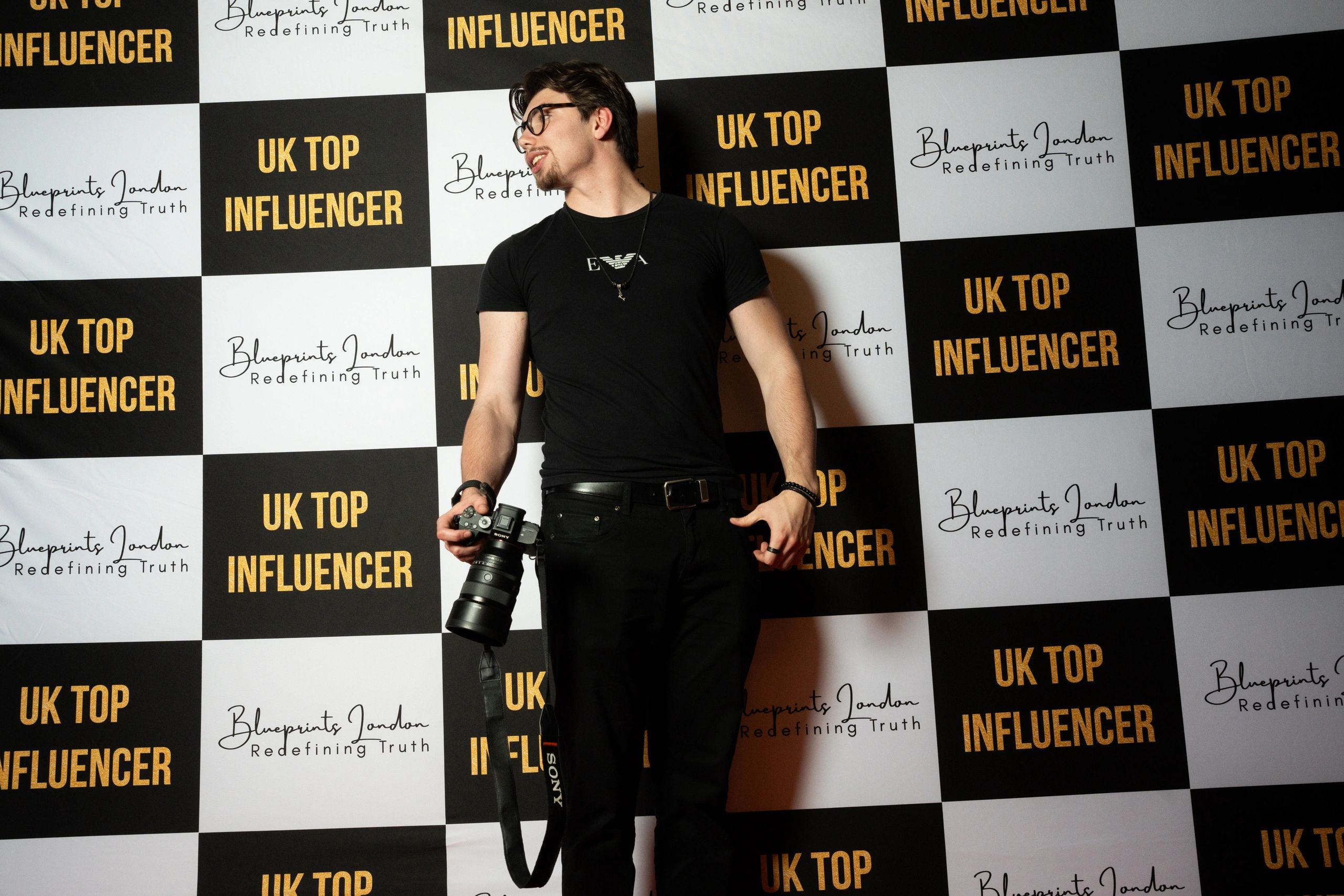 Man with a camera poses in front of UK Top Influencer backdrop.